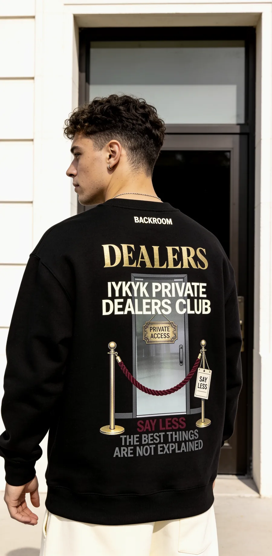 Model wearing a black Dealers sweatshirt in front of a doorway
